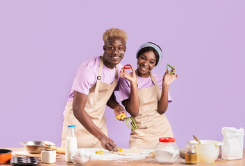 Attractive African American girlfriend and boyfriend making cookies on lilac background