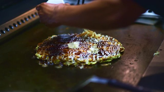 Okonomiyaki - Japanese cabbage pancake version of Potato Latkes (Traditional Jewish Hanukkah food) Asian chef hands garnish japanese vegetarian pizza  with cheese and green coriander, closeup footage 