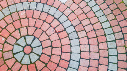 Round square area paved with red grey stones . Concentric lines of road tiles cover top view. Circle pavement pattern.