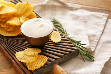 Board with tasty sour cream and potato chips on table