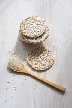 Aerial view of rice pancakes with raw white rice and wooden spoon, on white wooden table, vertical, with copy space