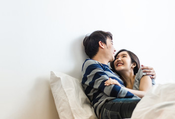 Happy & smiling attractive young cute Asian couple in love hugging and holding hands on bed in bedroom at home together. Happiness family of beautiful romantic married lover or marriage relationship