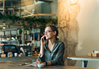 Smiling woman talking on smart phone. Businesswoman sitting at coffee shop and making a phone call.
