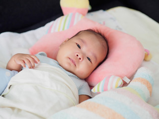 A cute Asian 2-month-old baby girl is lying down on a soft and comfortable mattress, with pillow and blanket. Close up shot.