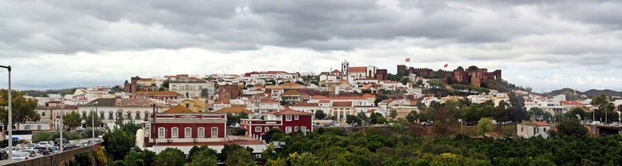 Fototapeta na wymiar Panorámica de Silves localizado en lo alto de la colina con el castillo medieval y catedral sobresaliendo sobre el resto de las casas del pueblo. Algarve, Portugal.