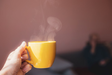 Yellow cup with hot streaming tea drink in hand