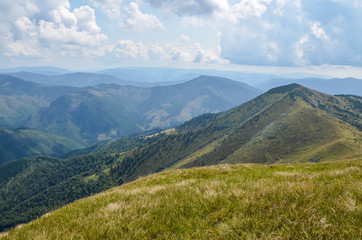 View of the Carpathian Mountains landscape in cloudy summer day. Mountain peaks, forests, fields and meadows, beautiful natural landscape.