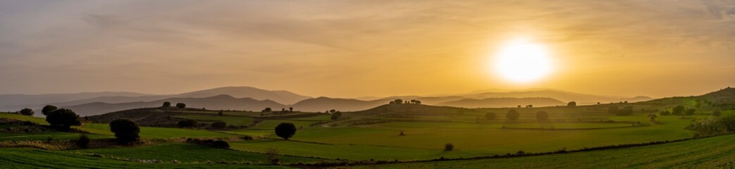 sunset panorama in the cereal fields view of valleys and mountains, warm colours and oranges, blues