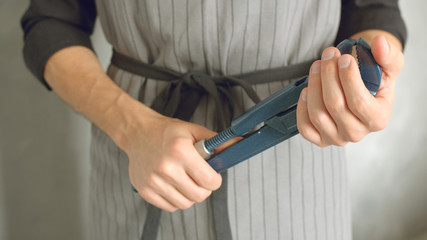 Close up of the hands of a worker or repairman in uniform holding a wrench against a gray background.