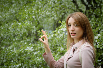 Obraz premium Blonde woman is showing ok on flowering tree background in the garden during early spring. Stop allergy concept