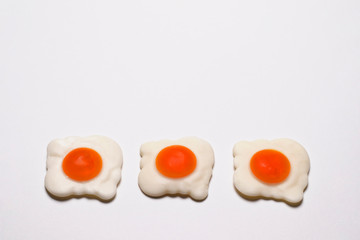 Three jelly-fried eggs lie in a horizontal line at the bottom of a white background. There is a place for text. An abstract photo was taken close-up for your design.
