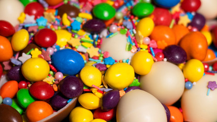 Many chocolate eggs and colored jelly candies of various sizes, strewn with colored sweet powder, were shot close-up. Custom size photo.