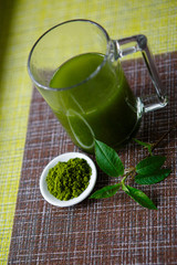 Japanese matcha green tea is poured into a white mug and on a white saucer in powder. Tea set on a textured napkin of natural flowers, decorated with a branch of green leaves. Background with space fo