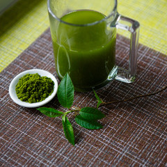 Japanese matcha green tea is poured into a white mug and on a white saucer in powder. Tea set on a textured napkin of natural flowers, decorated with a branch of green leaves. Background with space fo