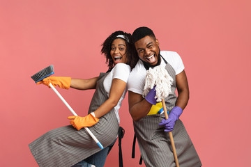 Positive black couple enjoying cleaning together, having fun with mop and broom