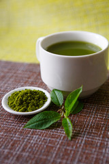 Japanese matcha green tea is poured into a white mug and on a white saucer in powder. Tea set on a textured napkin of natural flowers, decorated with a branch of green leaves. Background with space fo