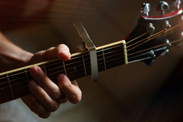The fingers of a man's hand on the neck of a guitar clamp the strings close-up. Guitar playing, beautiful lighting, background with space for text