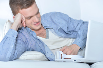 Handsome young man lying on white couch with laptop