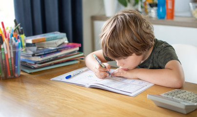 Boy learning at home in living room, writing something at the table