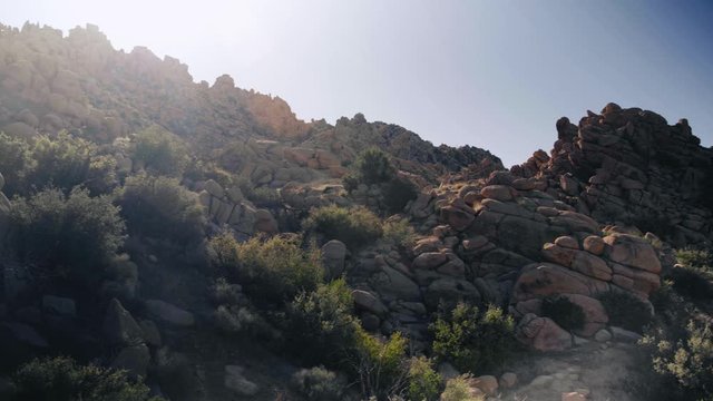 Panning shot of monzogranite rock formations on a hill in the desert at sunset.