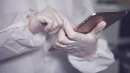 Close up of a nurse doctor or scientist using her ipad tablet tu research at the hospital laboratory wearing protective biohazard suit and gloves during coronavirus pandemic - Powered by Adobe