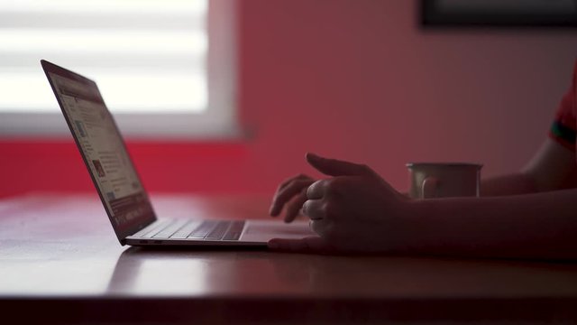Close up shot of hands browsing internet websites on laptop computer in low light dark room.