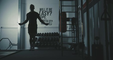 Male cross-fit athlete performs double unders with skipping jump rope inside a dark gym - Powered by Adobe
