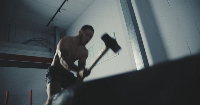 Young male fitness athlete hits a tyre with sledgehammer inside a gym