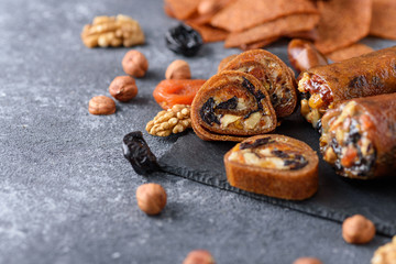 closeup fruit roll-up with nuts, prunes, dried apricots and honey, vegetarian snack, healthy bar on gray background, oriental sweets