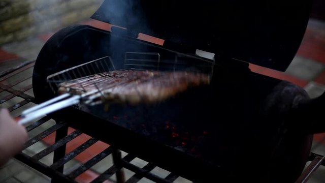 Cooking sausages in the grill. A man flips juicy meat sausages in a metal grate barbecue grill.