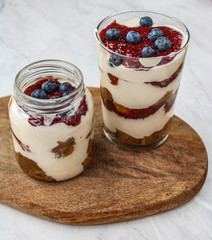 Healthy cheesecake in a glass and mason jar. Topped with fresh blueberries and made with homemade jam.  Cheesecakes place on top of a wooden board