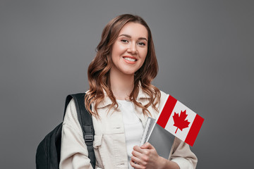 Young girl student smiling and holding a small canada flag isolated on dark gray background, Canada day, holiday, confederation anniversary, copy space