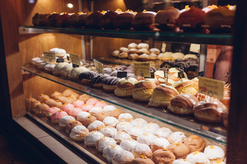 Assortment of doughnuts on cafe showcase. Variety of desserts with different flavours on shelves in store.