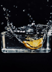 Lemon slice falling in glass square bowl, making a lot of splash around it.