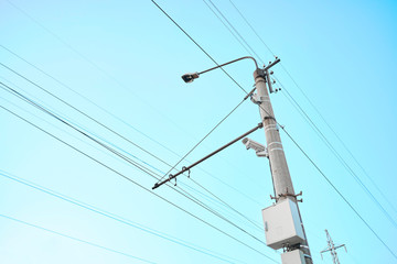 Outdoor surveillance camera on pole with cables. Against a bright blue sky background.