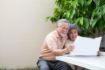 Happy Asian senior mature couple reading newspaper or magazine at front garden home