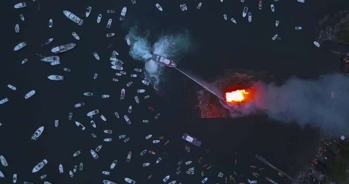 Unique, high altitude, top down, sideways flying drone footage of small motor boats and sail boats gathering around and witnessing the biggest bonfire event on Earth at Alesund, Norway at dusk.