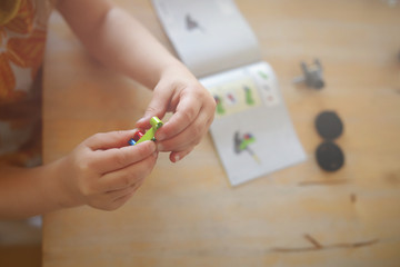 young girl in colorful dress puts togehter small parts with her little fingers to build a toy tractor from colorful plastic bricks  - bright light mood with heavily blurred background