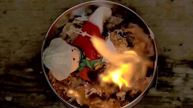 Sorcery witchcraft voodoo ritual with a doll being burned inside a bowl with fire to make a curse spell with him.  Mu&ntilde;eco de a&ntilde;o viejo.