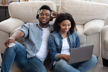 Black Couple Relaxing Together At Home, Listening Music And Using Laptop