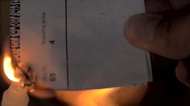 Holding an airplane ticket with one hand, while is being burned out with a candle.