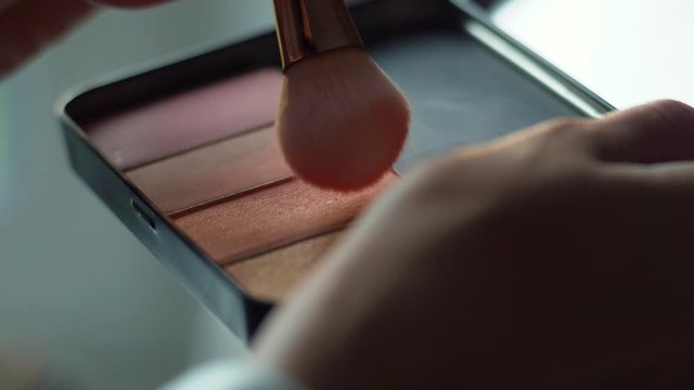 Soft brush wipes packs of color in makeup pallet to be applied to face of customer in salon. Wedding and beauty pageant preparation concept. Cosmetic application technique and product.
