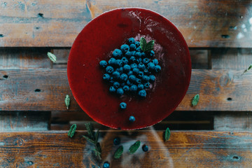 Blueberry cheesecake on a wood table, with some green leaves and blueberries on the side.