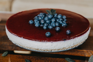 Blueberry cheesecake, with blueberries and red jelly on the top, green leaves and white cream.