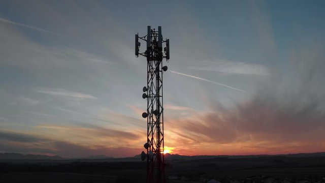 Drone fly closeup to 4G, 5G and microwave antenna of data telecom tower for smartphone and fast wireless internet during a sunset with mountain landscape and little town
