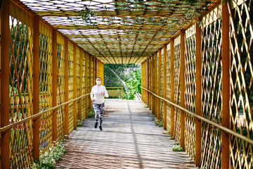 Athletic blonde woman with a mask on her face and a ponytail running on a yellow bridge. Running concept.