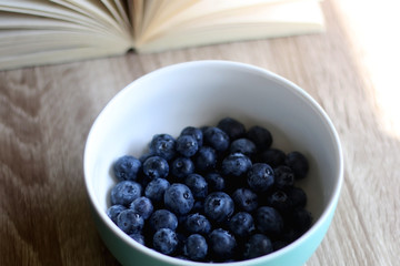 Bowl of fresh blueberries and open book on a table. Selective focus.