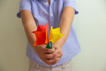 The boy holds in his hands flowers tulips made of paper which he donated by his mother’s day. DIY gif