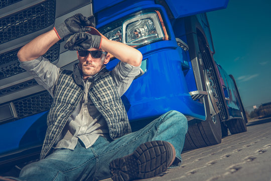 Male Trucker Sitting On Ground At Rest Stop Area.