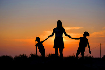 Fototapeta na wymiar Mother and children hold hands in the background of the sunset.